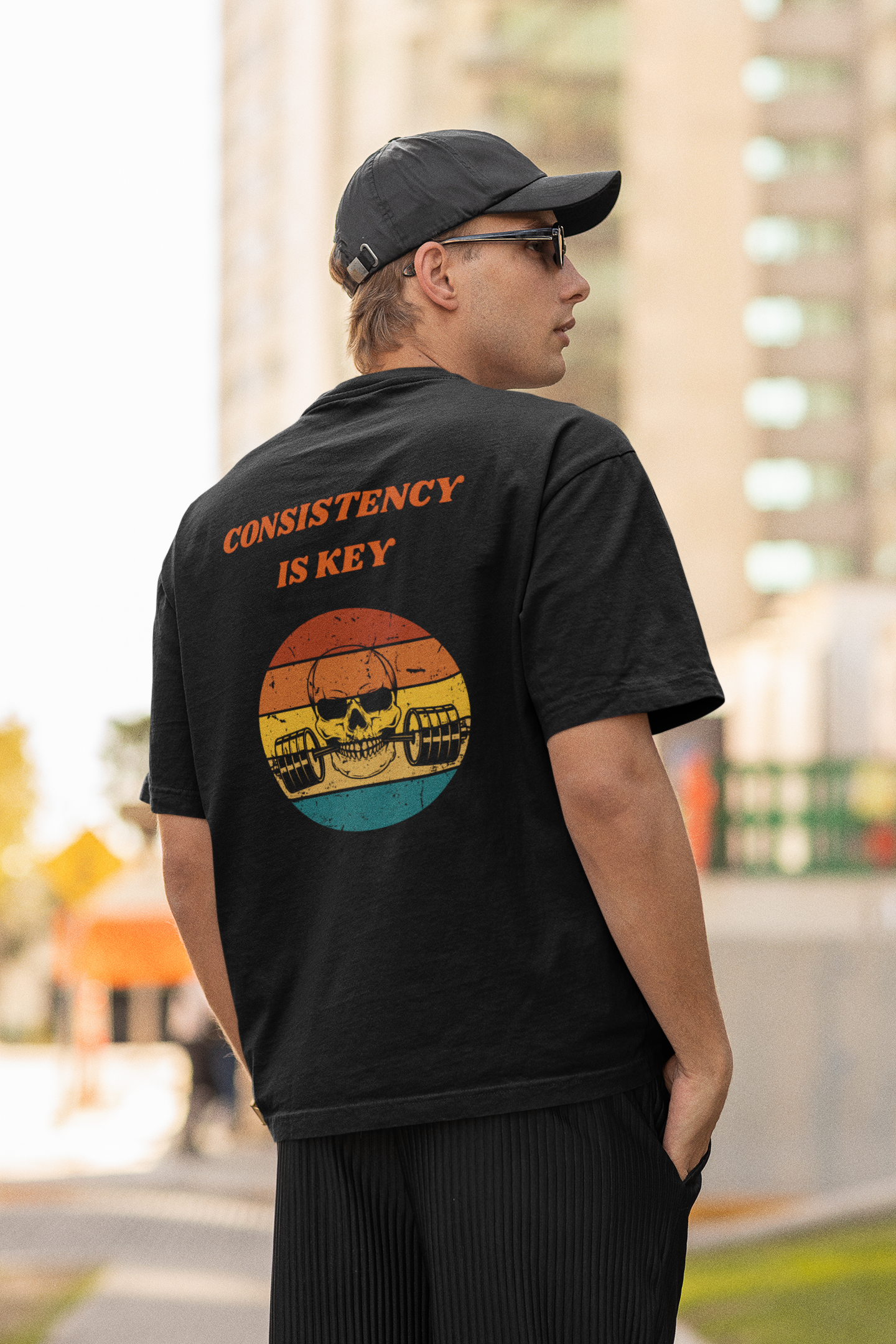 Back view of a man wearing a dark oversized "Consistency Is Key" retro skull gym t-shirt.