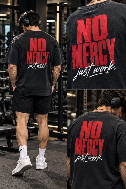 Male model showing the back of a black oversized T-shirt with red No Mercy and white Just Work lettering in a gym.