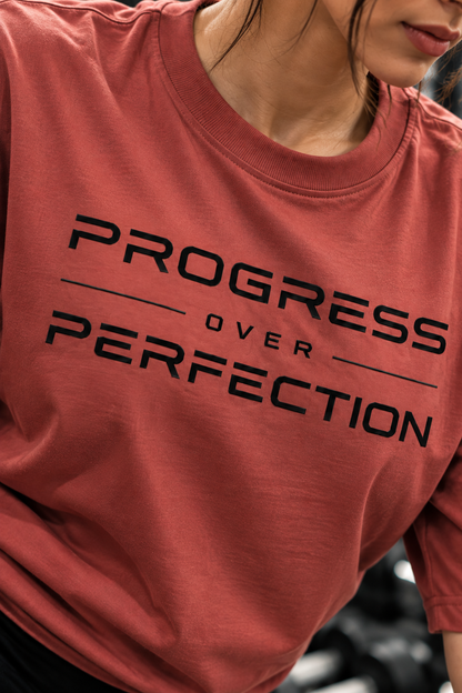 Detailed closeup of black Progress Over Perfection lettering on a muted red T-shirt