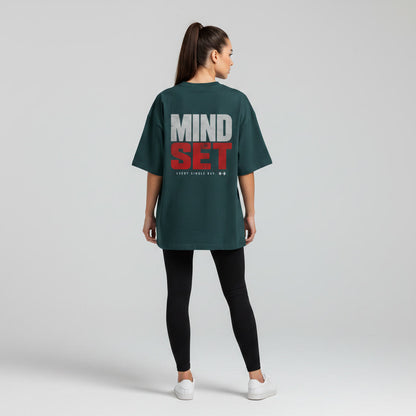 Back view of woman wearing dark green Mind Set oversized T-shirt with motivational back print