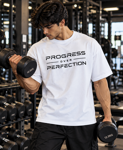 Man wearing a white Progress Over Perfection oversized T-shirt while doing a dumbbell curl in the gym